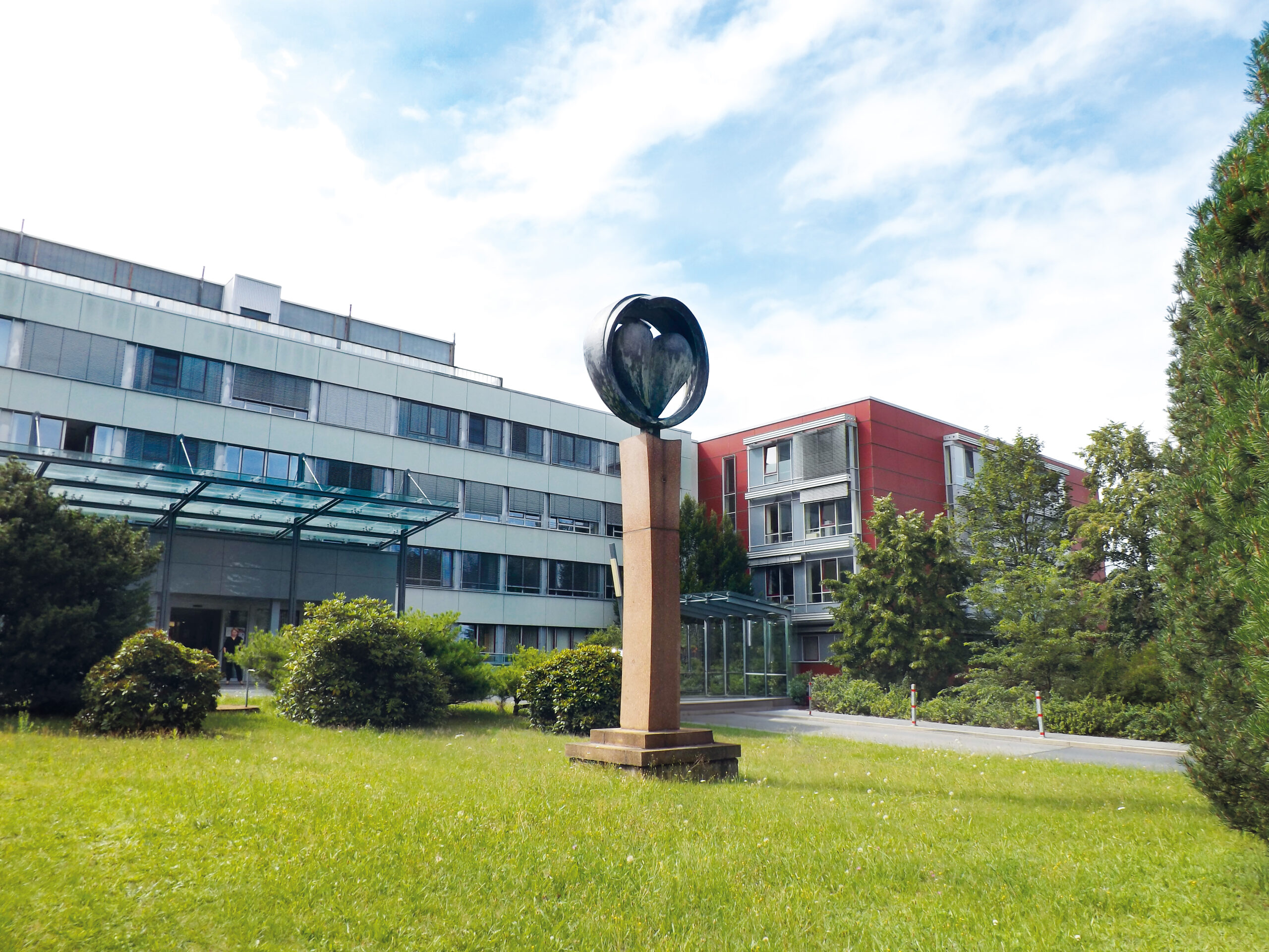 Eingang des Kreiskrankenhauses mit Blick auf Herzstatue und Bettenhaus